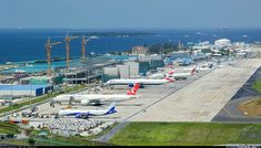 an airport with several planes parked on the tarmac and water in the back ground