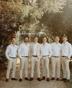 a group of men standing next to each other in front of some trees and bushes