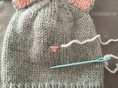 a knitted cat hat with yarn on it and a knitting needle next to it