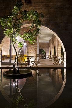 an indoor swimming pool at night with chairs and trees in the center, surrounded by brick walls