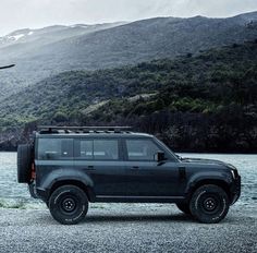 a black land rover parked next to a lake with mountains in the backgroud