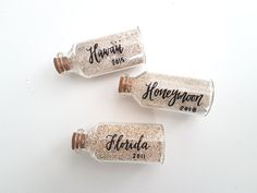 three personalized glass bottles with corks on the top, one filled with sand