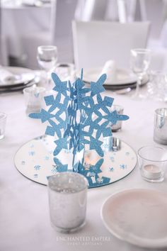 a table set with plates, silverware and blue paper snowflake centerpieces