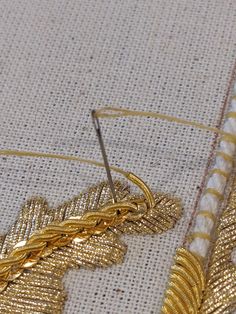 closeup of gold colored thread and golden leaves on white fabric with scissors in the foreground