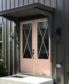 a pink double door on the side of a metal building next to bushes and shrubbery