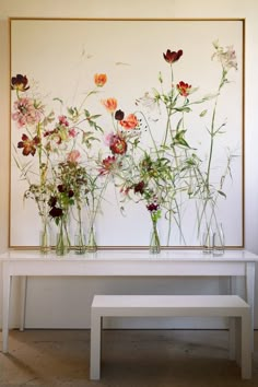 three vases with flowers are sitting on a white bench in front of a painting