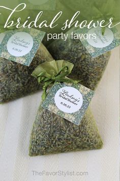 three bags of wedding shower party favors with green ribbons and tags on the top, sitting on a white table cloth