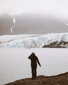 a man standing on top of a hill next to a body of water with a glacier in the background