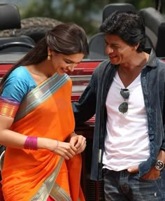 a man and woman standing next to each other in front of a red car with the door open