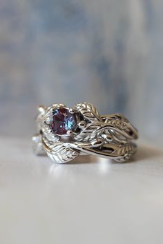 two silver rings with blue topazte and leaves on the sides, sitting on a white surface