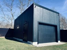 a black garage sits in the middle of a yard