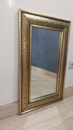 a gold framed mirror sitting on top of a hard wood floor next to a wall