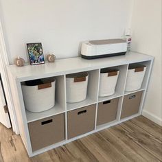 a white shelf with several bins and a microwave on top in a room that has wood flooring