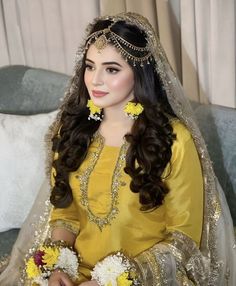 a woman sitting on a couch wearing a yellow dress with flowers in her hair and jewelry