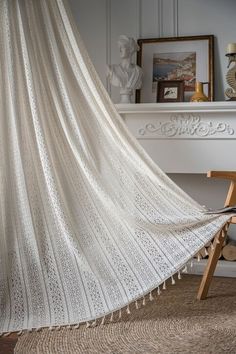 a white bed sitting next to a fireplace covered in a white lace curtain with tassels