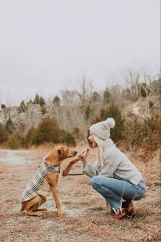 a woman kneeling down petting a dog on top of a dry grass covered field