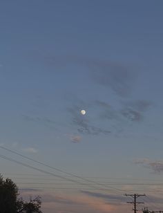 the full moon is seen in the sky above power lines and telephone poles at dusk