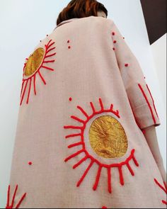 a woman is wearing a pink coat with red trims and gold sun designs on it