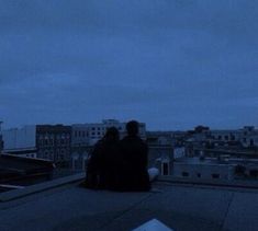 two people sitting on top of a roof at night