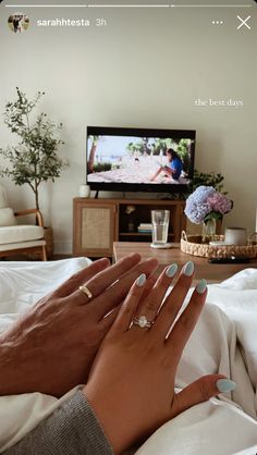 two hands holding each other while sitting on a bed in front of a flat screen tv