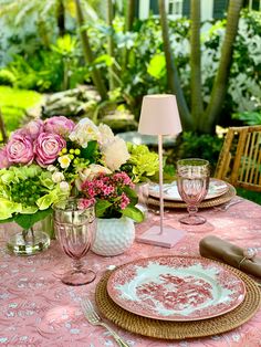 the table is set with pink and white flowers in vases, plates, and utensils