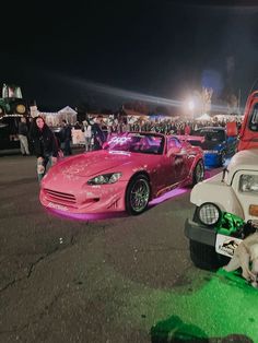 several cars parked in a parking lot at night with people standing around and one dog laying on the ground