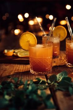 two glasses filled with drinks sitting on top of a wooden table next to lemon slices