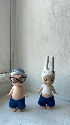 two toy figurines sitting next to each other on a window sill in front of a white wall