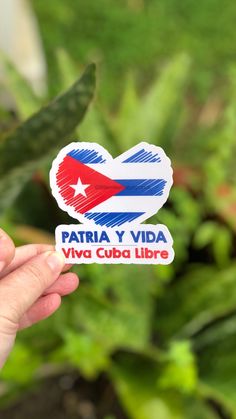 a person holding up a sticker with the flag of cuba on it in front of some plants