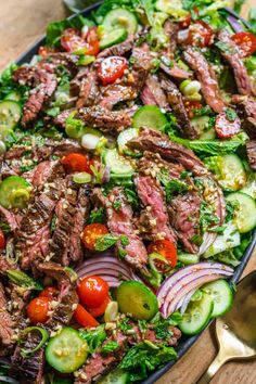 steak salad with tomatoes, cucumbers and onions in a black bowl on a wooden table