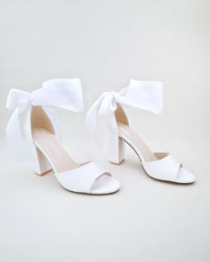 a pair of white high heeled shoes with a bow