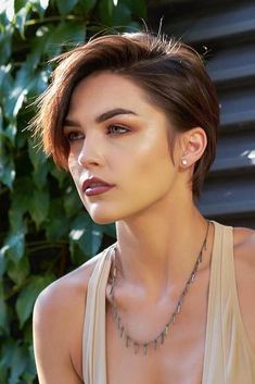 a woman with short hair wearing a tan tank top and silver necklace on her neck