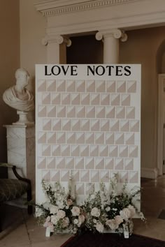 a large love notes board with flowers on the floor in front of a marble statue