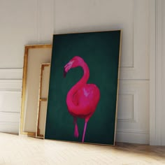 a pink flamingo standing in front of a green wall with two framed pictures on it