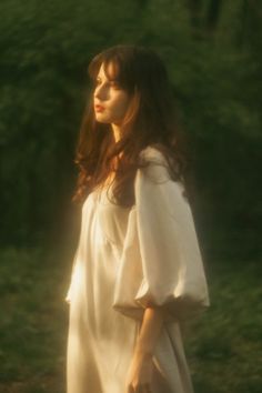 a woman in a white dress is walking through the grass with her hand on her hip