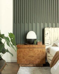 a bed room with a neatly made bed next to a nightstand and a plant in the corner