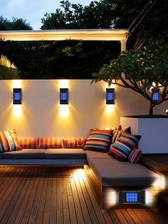 an outdoor seating area with lights on the wall and wooden flooring in front of it