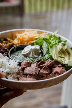 a person holding a bowl filled with meat, rice and veggies