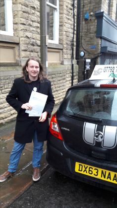 a woman standing next to a parked car on the side of a street holding papers