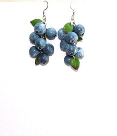 blueberries with green leaves are hanging from silver earwires on a white surface