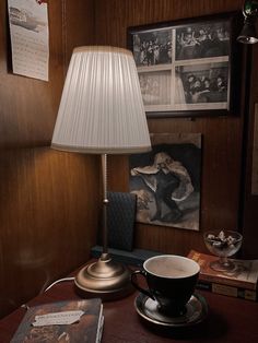 a lamp on a table next to a cup and book in a room with wood paneling