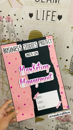 a person holding up a pink and black book with the words marketing management written on it