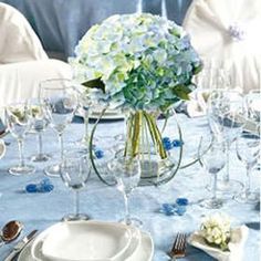 the table is set with white and blue flowers in vases, silverware, and wine glasses