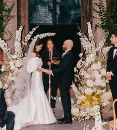 a bride and groom standing at the alter during their wedding ceremony in front of an arch decorated with white flowers