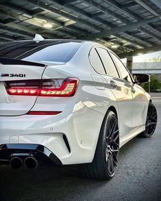 the rear end of a white bmw car parked in a garage with its lights on