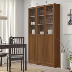 a dining room with a table and chairs next to a tall wooden bookcase filled with glasses