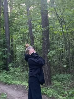 a woman standing in the middle of a forest talking on a cell phone while holding her hand up to her ear