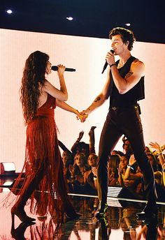 two people on stage with microphones and one person holding the other's hand