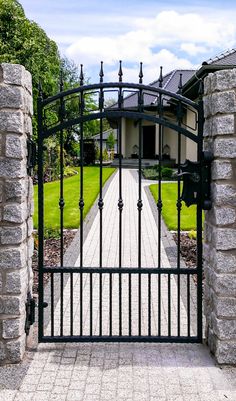 an iron gate in front of a house with stone pillars and brick walkway leading into the yard