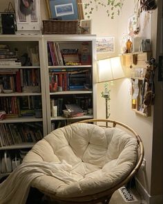 a chair that is in front of a book shelf with books on it and a lamp next to it